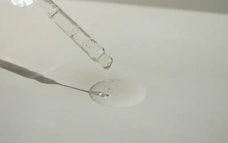 Clear watery hyaluronic acid serum being dispensed from a glass